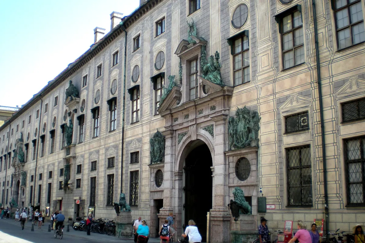 Dlouhé západní průčelí mnichovské Rezidence na Residenzstraße se kamenným portálem, po jehož stranách stojí bronzoví lvi.