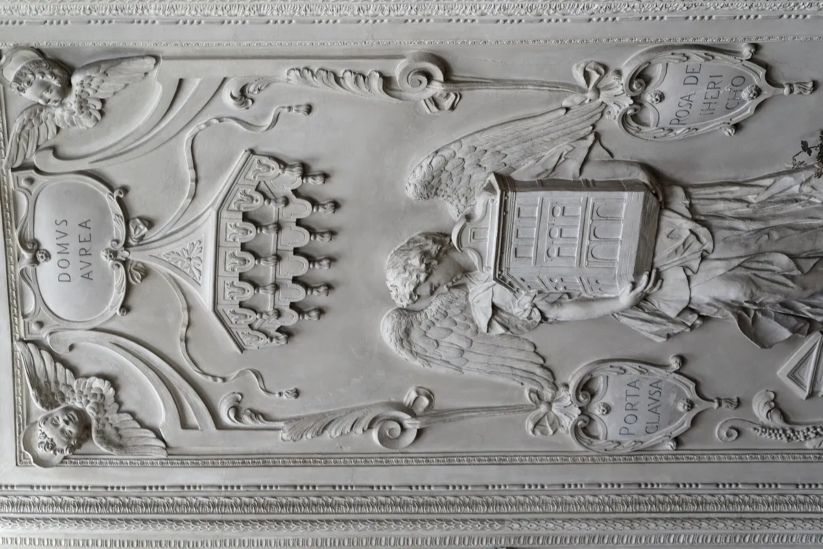 Štukový panel v kapli s erby, anděly a ornamenty v bílém reliéfu.