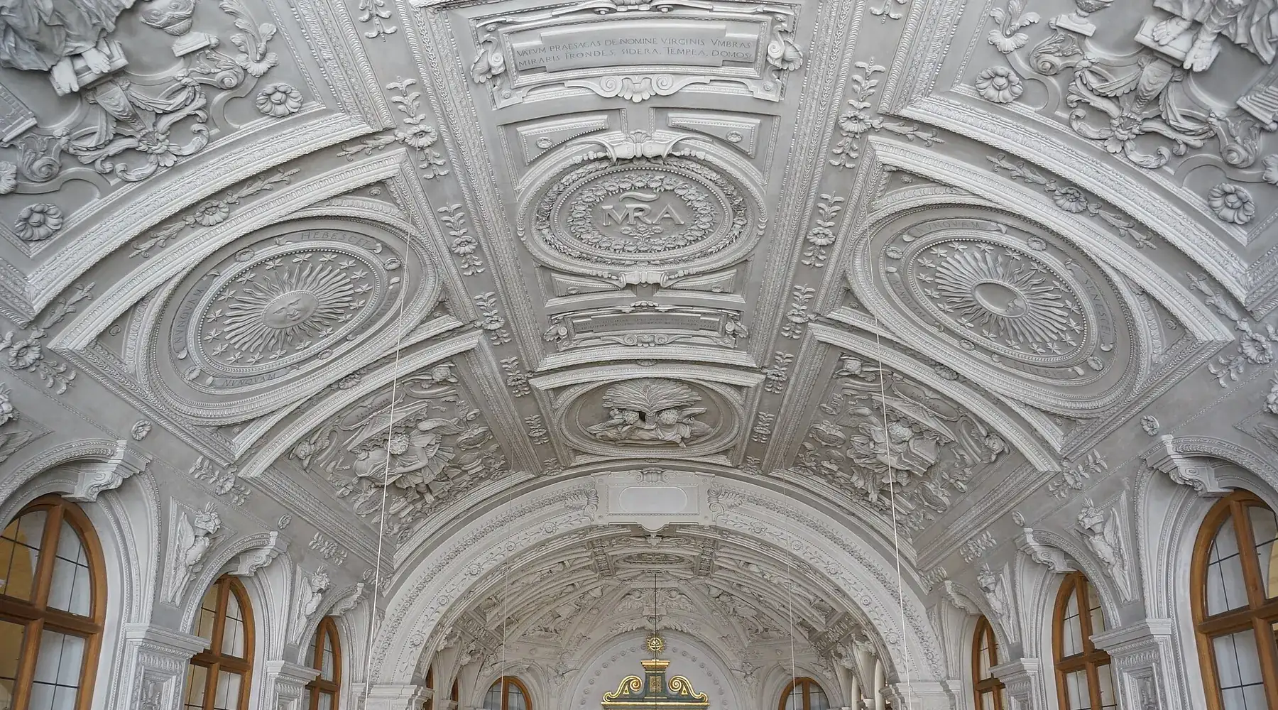 Klenba dvorní kaple pokrytá bílými štukovými žebry, oválnými medailony a reliéfními ornamenty, s obloukovými okny pod nimi.